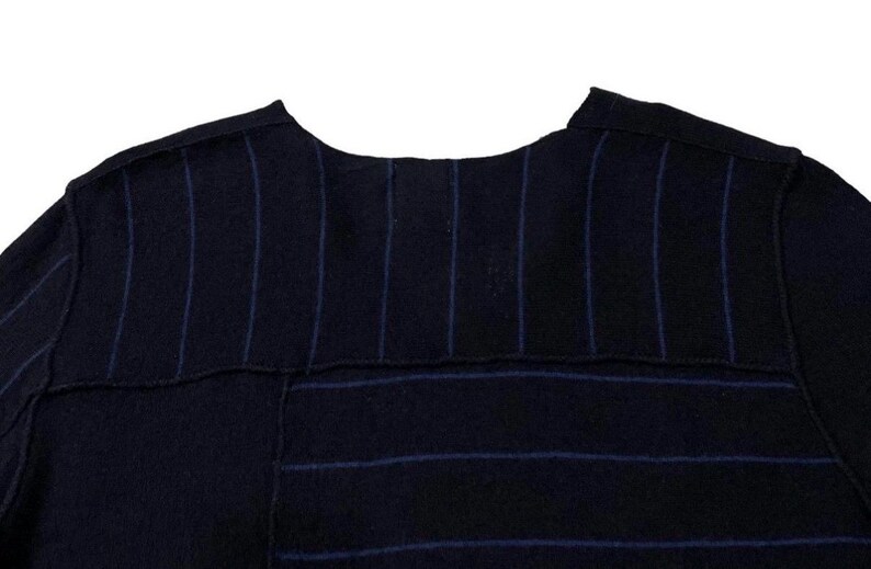 Puede incluir: Primer plano de una prenda azul marino con rayas azules verticales y horizontales. La tela parece ser un material texturizado, posiblemente lana. La prenda tiene un escote redondo.