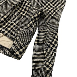 May include: Black and white patterned jacket with a classic houndstooth design. The jacket features a tailored fit with a visible sleeve and frayed edges. The interior lining is a light beige color.