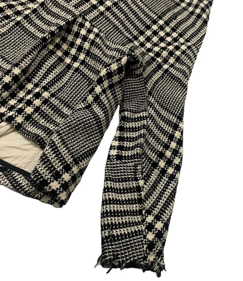 May include: Black and white patterned jacket with a classic houndstooth design. The jacket features a tailored fit with a visible sleeve and frayed edges. The interior lining is a light beige color.