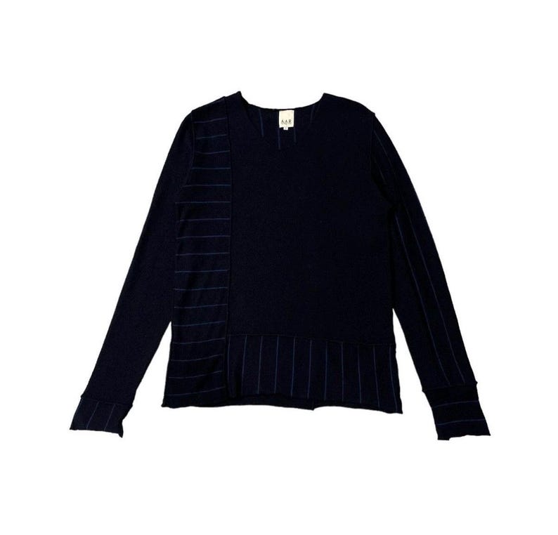 Puede incluir: Camisa de manga larga azul marino con cuello en V. La camisa presenta detalles de rayas verticales en el lado izquierdo y en la manga derecha. El dobladillo inferior tambi&eacute;n tiene detalles de rayas horizontales. Una peque&ntilde;a etiqueta est&aacute; cerca del cuello.