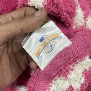 May include: Close-up of a pink and white patterned towel with a tag that reads "Universal Studios Japan". The towel is made of a soft, plush material.