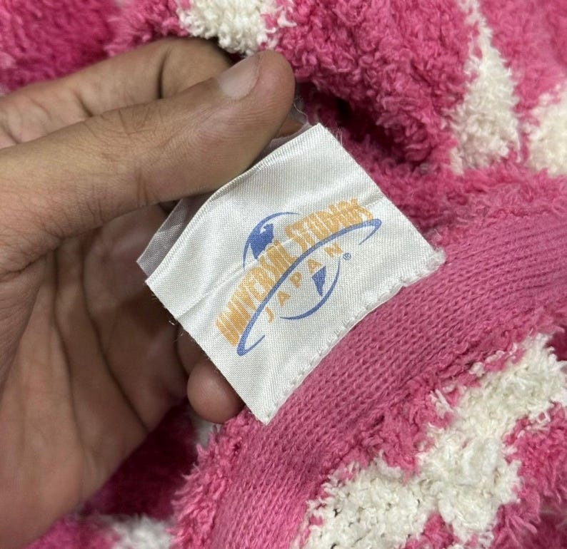 May include: Close-up of a pink and white patterned towel with a tag that reads "Universal Studios Japan". The towel is made of a soft, plush material.