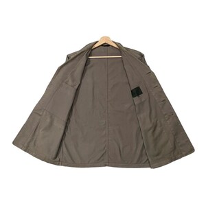 May include: A khaki-colored jacket is displayed open, revealing the interior lining and pockets. The jacket is hanging on a wooden hanger against a white background. The jacket has a classic design with a collar and button closures.