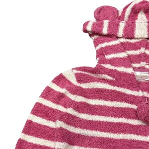May include: A pink and white striped hooded onesie with a pom-pom zipper pull. The hood features two small, rounded ear-like details. The onesie is made of a soft, plush material, perfect for lounging or sleepwear.