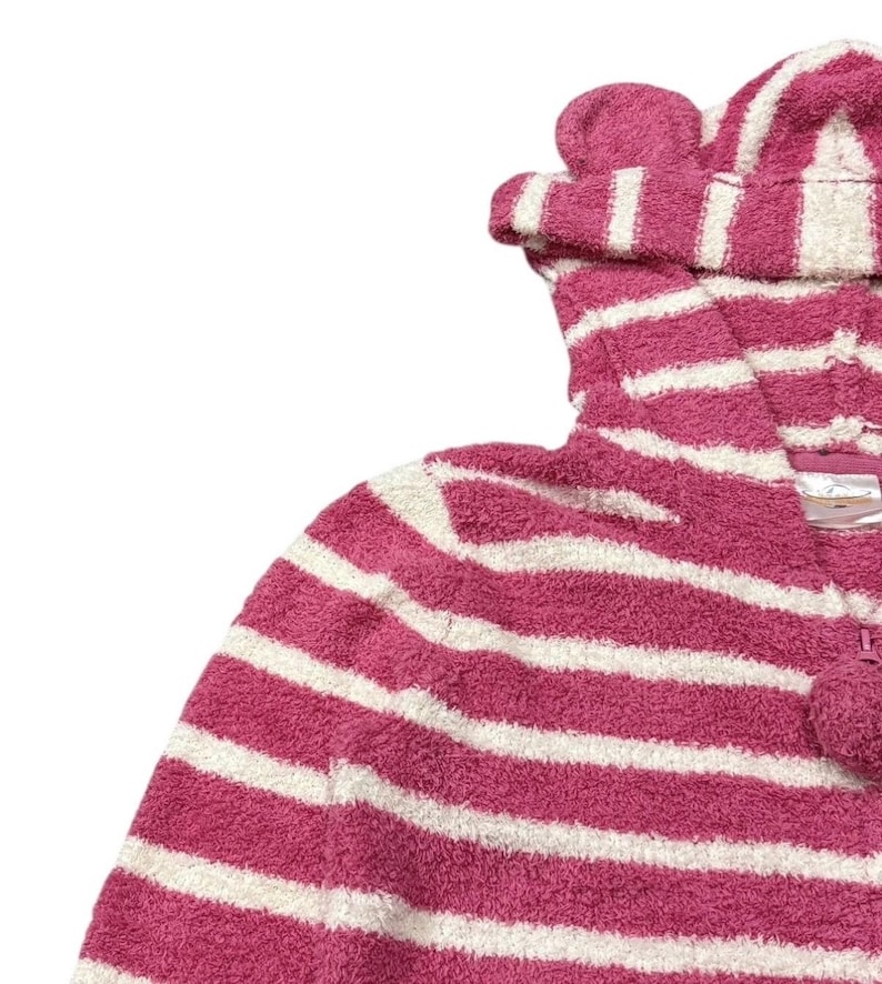 May include: A pink and white striped hooded onesie with a pom-pom zipper pull. The hood features two small, rounded ear-like details. The onesie is made of a soft, plush material, perfect for lounging or sleepwear.