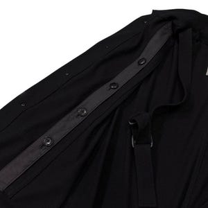 May include: Black jacket with a button-up closure and a strap detail. The jacket features a dark gray strip with buttons and a label on the inside. The fabric appears to be a lightweight material.