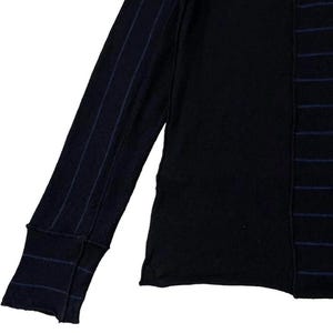 Puede incluir: Camiseta negra de manga larga con un dise&ntilde;o &uacute;nico. Una manga presenta finas rayas azul marino, mientras que el cuerpo tiene rayas verticales azul marino. La camiseta tiene un pu&ntilde;o acanalado y cuello redondo. Una parte superior elegante y c&oacute;moda para el uso diario.