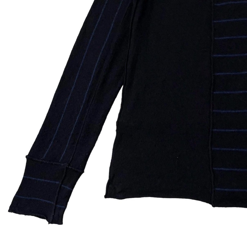 Puede incluir: Camiseta negra de manga larga con un dise&ntilde;o &uacute;nico. Una manga presenta finas rayas azul marino, mientras que el cuerpo tiene rayas verticales azul marino. La camiseta tiene un pu&ntilde;o acanalado y cuello redondo. Una parte superior elegante y c&oacute;moda para el uso diario.