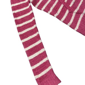 May include: A pink and white striped sweater sleeve. The sweater has a soft, fuzzy texture and a ribbed cuff. The stripes are horizontal and evenly spaced.