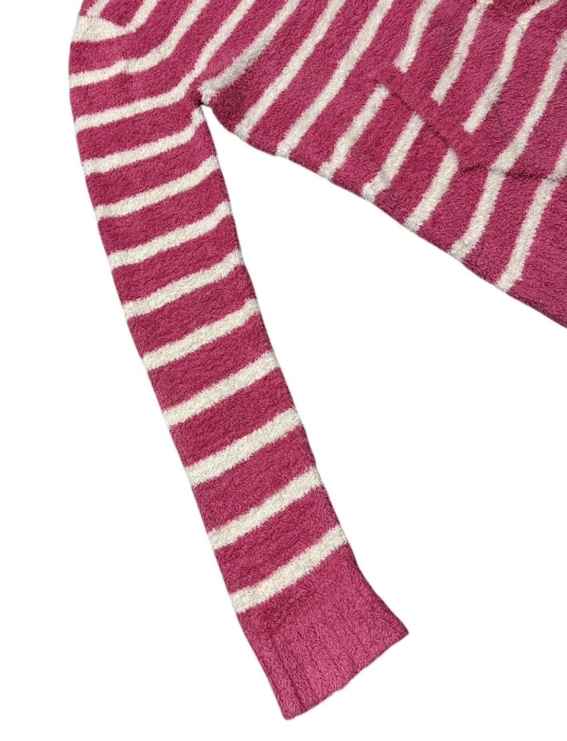 May include: A pink and white striped sweater sleeve. The sweater has a soft, fuzzy texture and a ribbed cuff. The stripes are horizontal and evenly spaced.