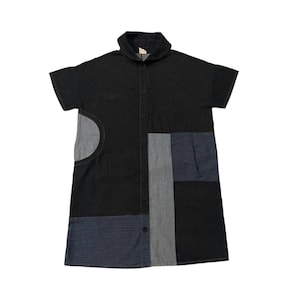 May include: Black collared dress with short sleeves and a button-down front. The dress features patchwork panels in shades of grey and blue, with a unique circular design on the left side.