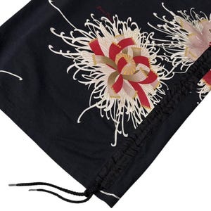 May include: Black fabric with a floral design featuring red, white, and gold accents. The design includes a drawstring closure with black cord and metal aglets. The fabric is folded, showing the pattern.