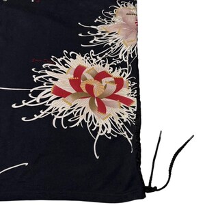 May include: Black drawstring bag with a floral pattern. The design features large, stylised flowers in red, white, and pink, with delicate white lines on a black background. The bag has black drawstrings.