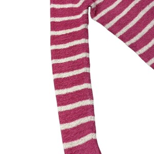 May include: A close-up of a pink and white striped sweater sleeve. The sleeve is made of a soft, textured material. The stripes are horizontal and evenly spaced. The cuff is a solid pink color.