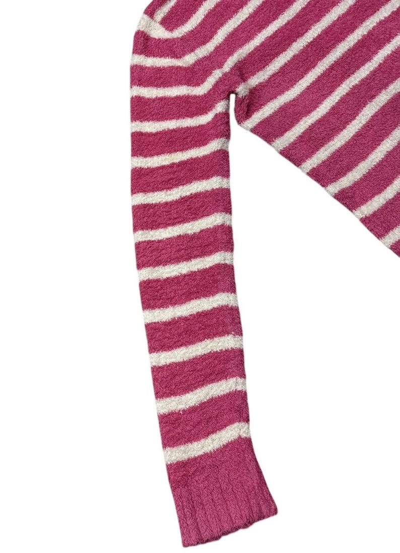 May include: A close-up of a pink and white striped sweater sleeve. The sleeve is made of a soft, textured material. The stripes are horizontal and evenly spaced. The cuff is a solid pink color.