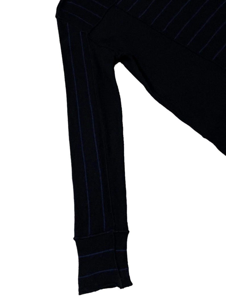 Puede incluir: Camisa negra de manga larga con finas rayas verticales azul marino. El pu&ntilde;o de la manga es visible, tambi&eacute;n con rayas azul marino. La camisa est&aacute; hecha de un material suave y c&oacute;modo.