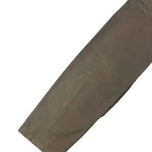 May include: Close-up of a section of olive-green pants. The fabric appears to be a sturdy material, with visible seams and a slight sheen. The pants are angled, showing the leg and hem.