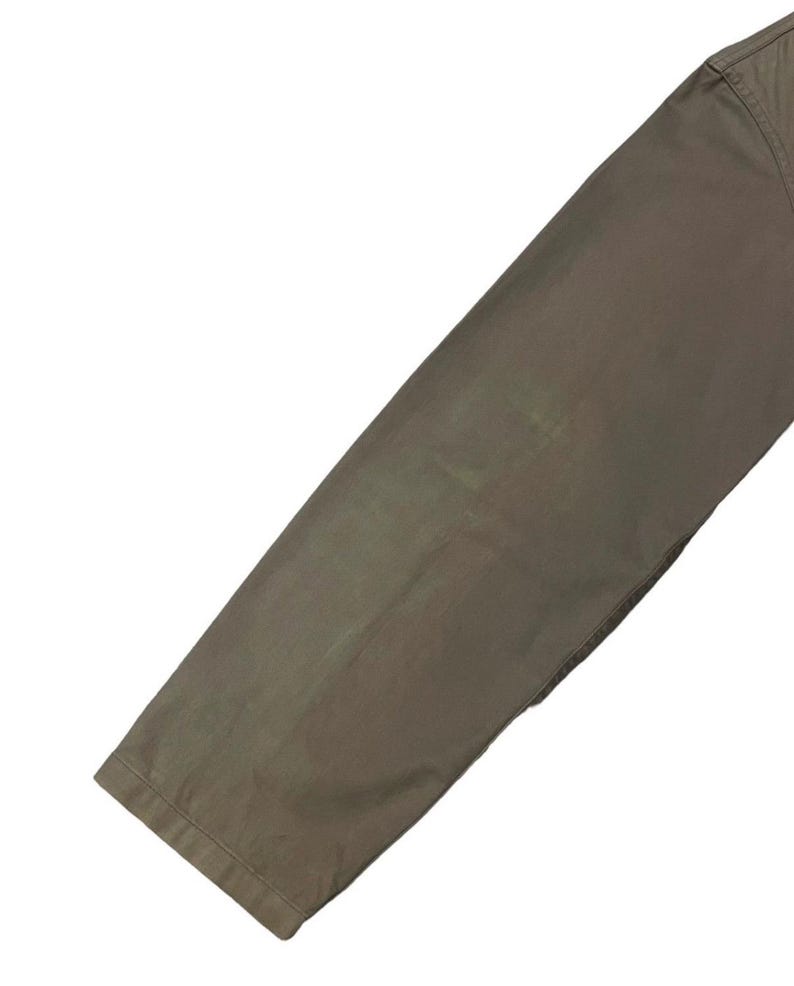 May include: Close-up of a section of olive-green pants. The fabric appears to be a sturdy material, with visible seams and a slight sheen. The pants are angled, showing the leg and hem.
