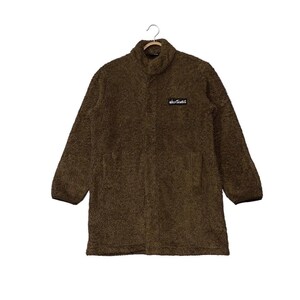 May include: A brown, long-sleeved coat with a high collar and two front pockets. The coat has a fuzzy texture and a small rectangular patch with white text. The coat is hanging from a wooden hanger.