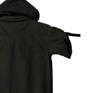 Puede incluir: Chaqueta negra con capucha y mangas cortas. La chaqueta tiene capucha, cierre de botones en la parte delantera y un corte entallado. Las mangas son cortas y la chaqueta parece estar hecha de una tela duradera. El estilo general es casual y pr&aacute;ctico.