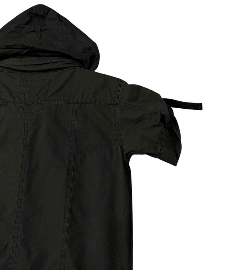 Puede incluir: Chaqueta negra con capucha y mangas cortas. La chaqueta tiene capucha, cierre de botones en la parte delantera y un corte entallado. Las mangas son cortas y la chaqueta parece estar hecha de una tela duradera. El estilo general es casual y pr&aacute;ctico.