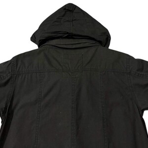 Puede incluir: Chaqueta negra con capucha y mangas cortas. La chaqueta tiene capucha, cierre de botones en la parte delantera y correas ajustables en las mangas. La parte trasera de la chaqueta es visible, mostrando los detalles de las costuras y el dise&ntilde;o general.