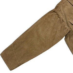 K&ouml;nnte beinhalten: Nahaufnahme eines tan-farbenen Cordjacken&auml;rmels. Der &Auml;rmel ist angewinkelt und zeigt die gerippte Textur des Stoffes. Die Jacke hat eine Tasche und eine gekn&ouml;pfte Manschette. Die Farbe ist ein warmer, erdiger Ton.