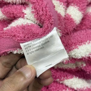 May include: Close-up of a pink and white striped towel. A white tag with text that reads "Universal Studios Japan and the Universal Globe Logo &copy; & &reg; Universal Studios. All rights reserved." is visible.