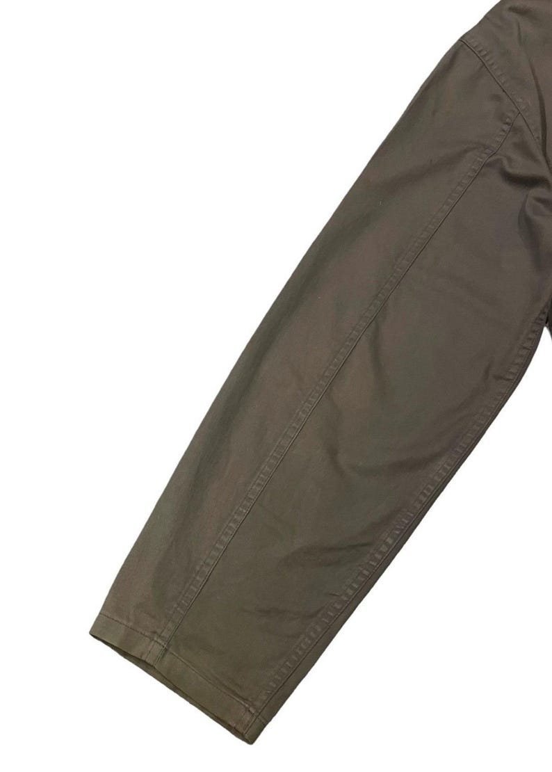 May include: Close-up of a section of a brown garment, likely a jacket or coat sleeve. The fabric appears to be a sturdy material, with visible stitching along the seams. The color is a muted, earthy brown.