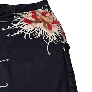 May include: Black garment with a floral design. The floral pattern features red, white, and gold colours. The garment has a black ribbed waistband and a black, textured side panel.