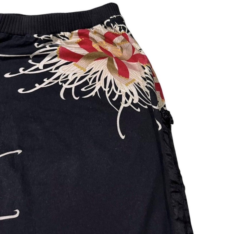 May include: Black garment with a floral design. The floral pattern features red, white, and gold colours. The garment has a black ribbed waistband and a black, textured side panel.
