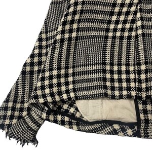 May include: Close-up of a black and white houndstooth patterned jacket. The jacket has a frayed edge and a light-colored lining. The fabric has a woven texture, and the pattern is a classic design.