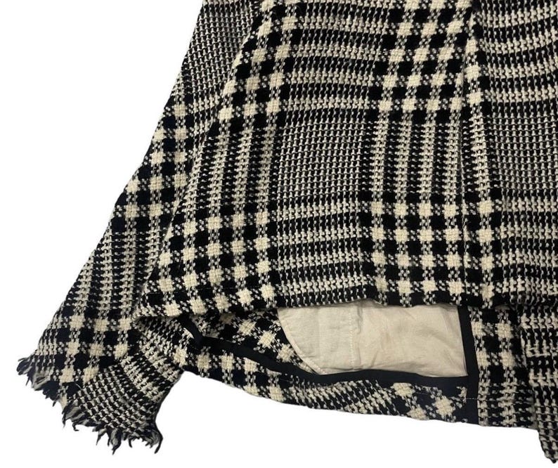 May include: Close-up of a black and white houndstooth patterned jacket. The jacket has a frayed edge and a light-colored lining. The fabric has a woven texture, and the pattern is a classic design.