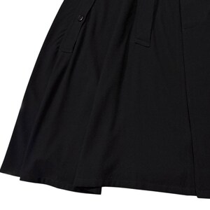 May include: A close-up of a black skirt with a button and a belt loop detail. The fabric appears to be a smooth, woven material. The skirt has a slight A-line shape.