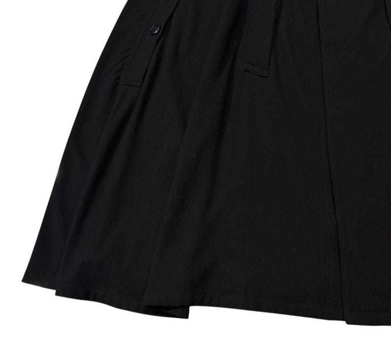 May include: A close-up of a black skirt with a button and a belt loop detail. The fabric appears to be a smooth, woven material. The skirt has a slight A-line shape.