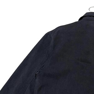 May include: A navy blue jacket with a collar and button closure, hanging on a metal hanger. The jacket's fabric appears to be a sturdy material, and the garment is viewed from the shoulder and upper arm.