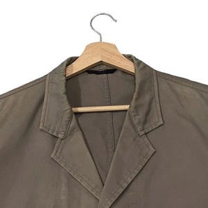 May include: A brown blazer with a notched lapel, hanging on a wooden hanger. The jacket has a classic design with a two-button closure and long sleeves. The fabric appears to be a medium-weight material, suitable for various occasions.