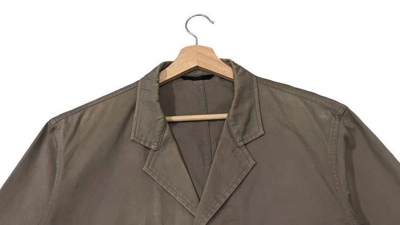 May include: A brown blazer with a notched lapel, hanging on a wooden hanger. The jacket has a classic design with a two-button closure and long sleeves. The fabric appears to be a medium-weight material, suitable for various occasions.