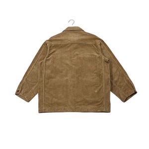 K&ouml;nnte beinhalten: Eine hellbraune Cordjacke, von hinten gesehen, h&auml;ngt an einem Metallhaken. Die Jacke hat einen Knopfverschluss, zwei Brusttaschen und lange &Auml;rmel. Der Stoff hat eine vertikale Rippenstruktur.