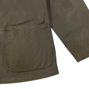 May include: Olive green jacket with a large front pocket and black buttons. The jacket has a classic design with a simple, functional aesthetic. The fabric appears to be a durable material, suitable for various weather conditions.