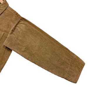 K&ouml;nnte beinhalten: Nahaufnahme eines tan-farbenen Cordjacken&auml;rmels. Der Stoff hat eine gerippte Textur und einen warmen, erdigen Ton. Die Jacke scheint neu zu sein, mit einem strukturierten Design und einer klassischen &Auml;sthetik. Der &Auml;rmel ist abgewinkelt und zeigt die Richtung des Stoffes.