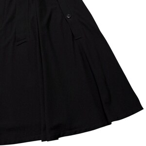 May include: A black skirt with a button closure and a pleated design. The skirt has a flowing, A-line silhouette, and is made of a smooth, opaque fabric. The skirt's hemline is visible in the image.