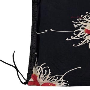 May include: Black drawstring bag with a floral pattern. The bag displays a repeating design of white and red flowers with cream accents. The drawstring is black, and the bag has a textured black border.