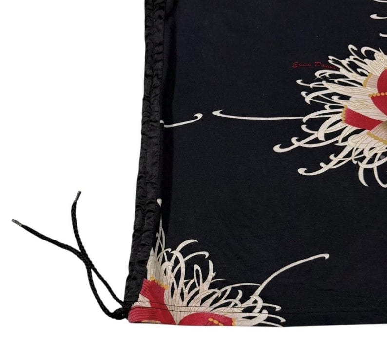 May include: Black drawstring bag with a floral pattern. The bag displays a repeating design of white and red flowers with cream accents. The drawstring is black, and the bag has a textured black border.