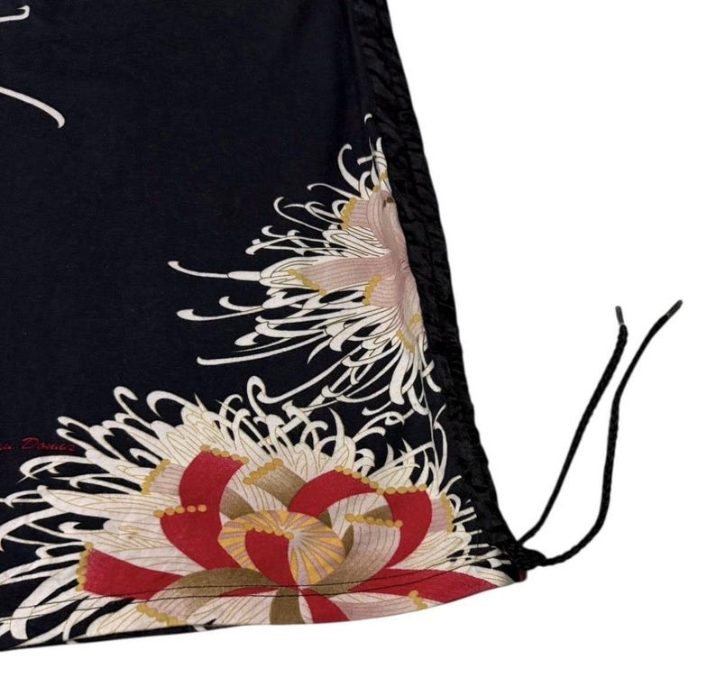 May include: Black fabric featuring a large floral design in red, white, and gold. The design is on the lower portion of the fabric. The fabric has a drawstring and a black trim.