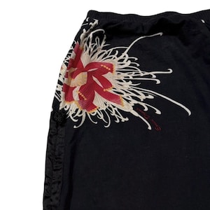 May include: Black trousers featuring a large floral design in red, cream, and yellow. The trousers have a drawstring waist and a decorative side seam. The floral design is on the upper left side.