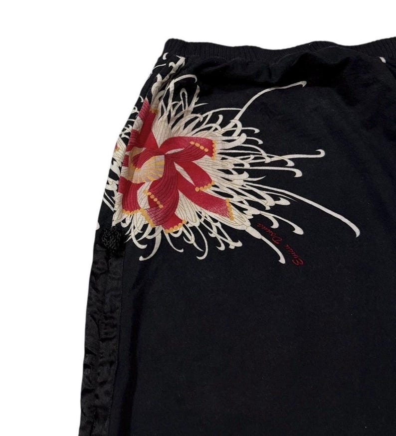 May include: Black trousers featuring a large floral design in red, cream, and yellow. The trousers have a drawstring waist and a decorative side seam. The floral design is on the upper left side.