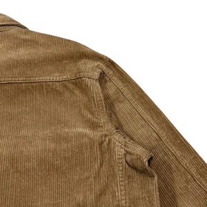 K&ouml;nnte beinhalten: Nahaufnahme einer braunen Cordjacke. Die Jacke hat einen klassischen Kragen, eine Brusttasche und eine Knopfleiste. Der Cordstoff hat eine gerippte Textur, und die Jacke scheint gut verarbeitet zu sein.