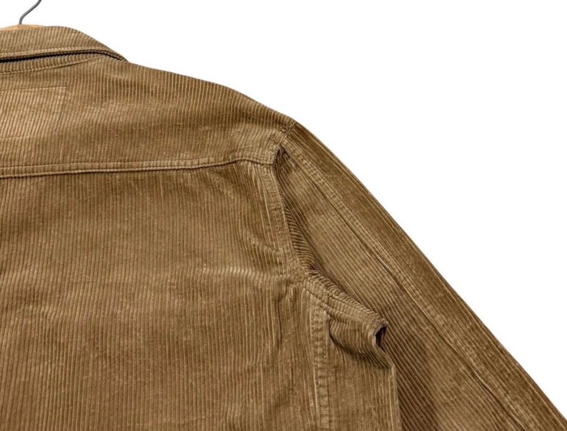 K&ouml;nnte beinhalten: Nahaufnahme einer braunen Cordjacke. Die Jacke hat einen klassischen Kragen, eine Brusttasche und eine Knopfleiste. Der Cordstoff hat eine gerippte Textur, und die Jacke scheint gut verarbeitet zu sein.