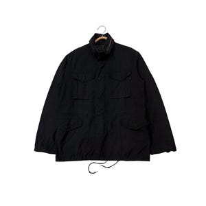 Peut inclure: Veste noire de style militaire avec plusieurs poches avant et un col montant. La veste est suspendue à un cintre sur fond blanc. Elle comporte un cordon de serrage à la taille et une fermeture éclair.